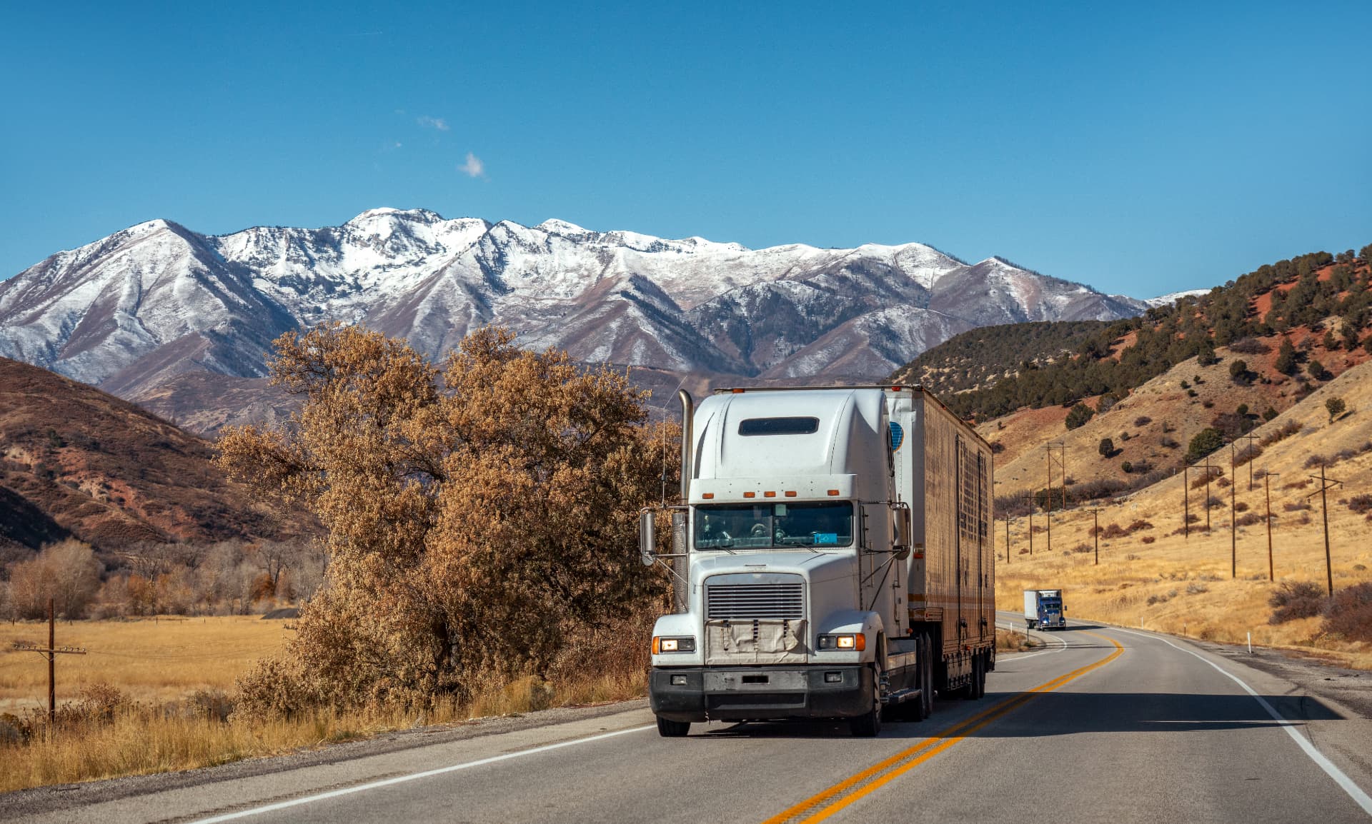 White semi-truck driving on a highway with snowcapped mountains in the background